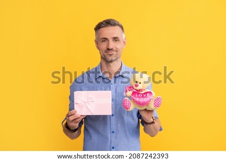 happy grizzled guy holding box and toy on yellow background, love
