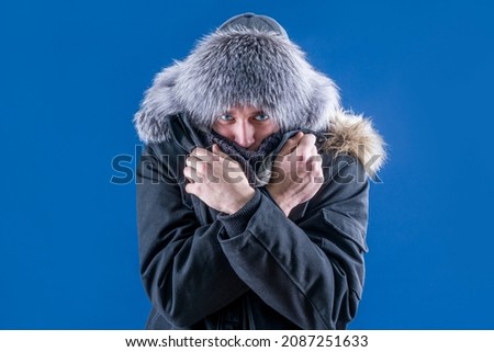 A man in a fur hat and warm clothes crossed his arms to keep warm. Freeze in winter. Snowfall. Winter.