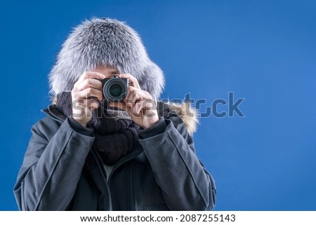 The photographer takes pictures of a beautiful winter. Photograph snow. A man in winter clothes holds a camera in his hands. Snowfall.