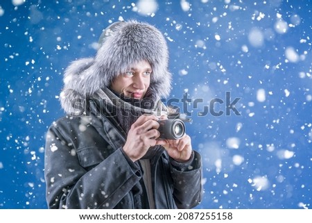 A man in winter clothes smiles and holds a camera in his hands. The photographer takes pictures of the beautiful winter. Snowfall. Take pictures of the snow