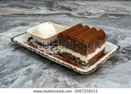 A slice of tiramisu and ice cream in a porcelain serving dish on a marble floor