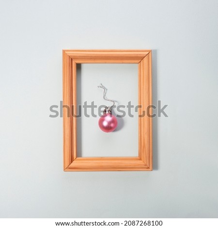 Christmas ball in a wooden photo frame on a pink background. creative minimalism christmas.
