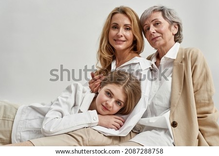 Portrait of three generations of Caucasian women on one picture. Smiling mother and mature grandmother protect little teen girl child. Isolated on white studio background. Family unity and bonding.