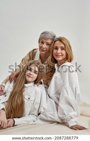 Vertical narrow portrait of smiling three generations of Caucasian women pose on white background in studio. Happy girl child with young mother and senior grandmother. Unity, motherhood. Royalty-Free Stock Photo #2087288779