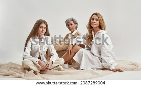 Portrait of happy beautiful three generations of Caucasian women pose on white studio background together. Teen girl child with young mother and old grandmother show family unity and bonding.
