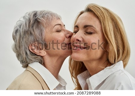 Close up of older Caucasian mother kiss in cheek smiling grownup daughter feel grateful thankful. Caring loving old mature mom and adult woman child have tender close family moment together.