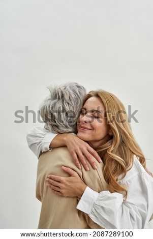Loving grownup daughter hug embrace old mother feel grateful and thankful, isolated on white studio background. Caring adult child cuddle mature mom. Vertical narrow shot. Motherhood. Royalty-Free Stock Photo #2087289100
