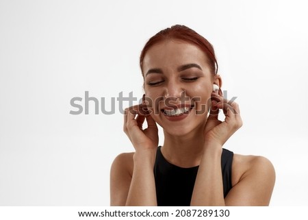 Joyful caucasian female ballet dancer with closed eyes listening music in earphones. Concept of modern technologies. Woman with red hair and wearing leotard. Isolated on white background in studio