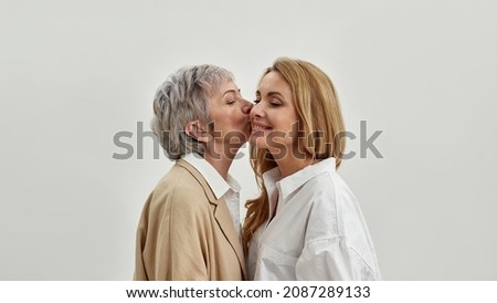 Old Caucasian mother kiss adult daughter in cheek show love and care, isolated on white studio background. Happy mature mom and grownup woman child tender family moment. Motherhood concept.