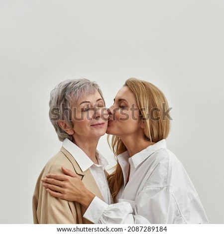 Loving adult daughter kiss happy mature mom in cheek feel grateful and thankful, isolated on white studio background. Caring grownup woman thank old mother for upbringing. Two generations.