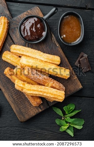 Traditional churros sticks with cinnamon and sugar powder set, on black wooden table background, top view flat lay
