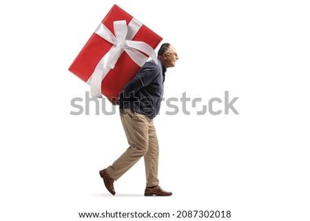 Full length profile shot of a mature man carrying a big wrapped present on his back isolated on white background