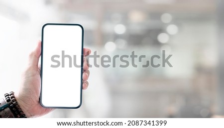 Cropped shot of businessman holding blank screen smartphone with blurred office room background.