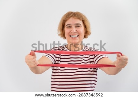 An elderly woman is engaged in fitness with an elastic band on a white background