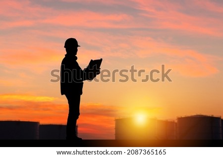 Silhouette of Engineer under inspection and checking oil storage tank, Engineer man in waistcoats and hardhats and with documents in oil storage plant Royalty-Free Stock Photo #2087365165