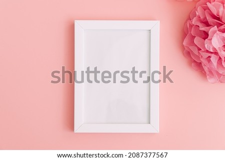 A white frame next to a pink flower on a pink background.