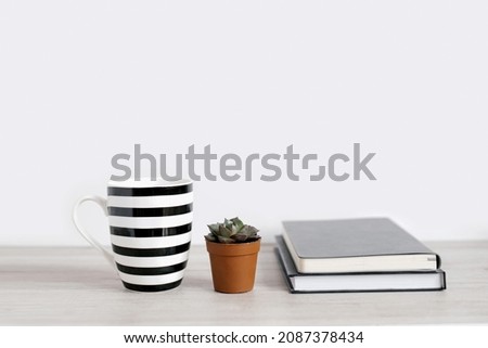 Black and white mugs on a table in a minimalist interior, business concept, succulent and notepads. Template, layout for your design, advertising, copy space.