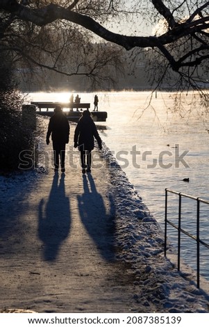 People walking on a walking path at Stockholm bay on freezing winter day with steaming water, birch tree in front and cozy sun light. Winter time in capital of Sweden  