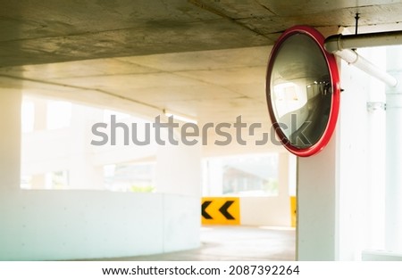 Convex safety mirror at curve of indoor car parking lot to reduce risk of accidents from blind corner or blind spots. Convex circular safety mirror in multi-level parking garage. Indoor traffic convex