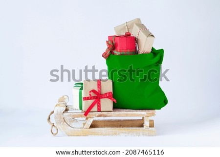 Santa Claus green bag full of christmas presents on wooden sleigh on light background stock image