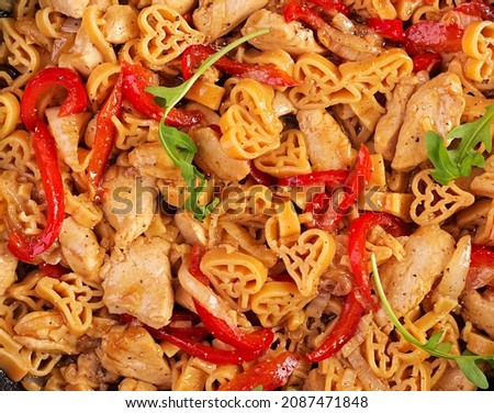 Heart-shaped pasta  in tomato sauce with chicken and sweet pepper with arugula. Background, texture