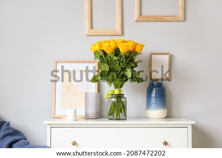 Vase with beautiful yellow roses on chest of drawers in interior of room