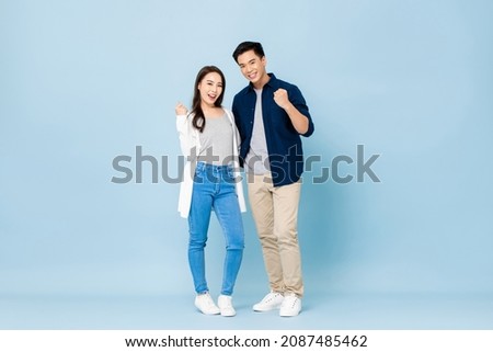 Full lenght portrait of young smiling Asian couple holding each other and clenching fists in isolated light blue studio background Royalty-Free Stock Photo #2087485462