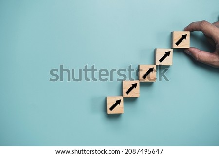 Hand putting increasing arrow which print screen on wooden cube block for business profit growth concept.