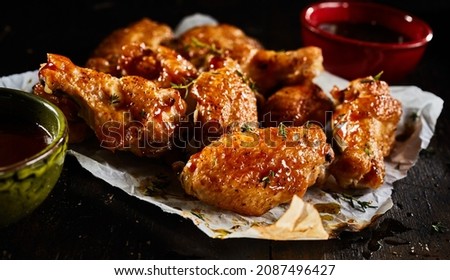 High angle of appetizing BBQ chicken wings with herbs served on paper on dark table with sauce in bowls in studio Royalty-Free Stock Photo #2087496427