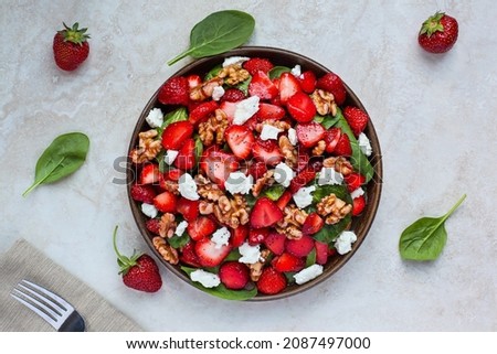 Flatlay of a plate of homemade fresh salad of baby spinach leaves, sliced strawberries, walnuts, feta cheese, and a light vinaigrette dressing.