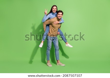 Photo of two funny people guy hold piggyback girlfriend show v-sign wear casual outfit isolated green color background