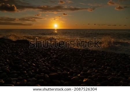 Sea waves roll on the pebble beach at sunset. A beautiful orange sunset with the sun going over the horizon of the sea, a pebble beach. Beautiful sunset background, seascape