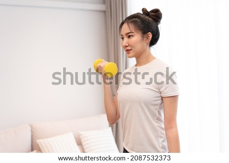 Productive activity concept a girl with a bun wearing a white t-shirt raising the yellow dumbbell with her right hand in her living space.