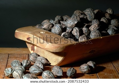 Wild walnuts on the rustic old table and in the wooden bowl. Ripe dry wild walnuts on the old wooden table, close-up, selective focus. Free space for text. A low key image.