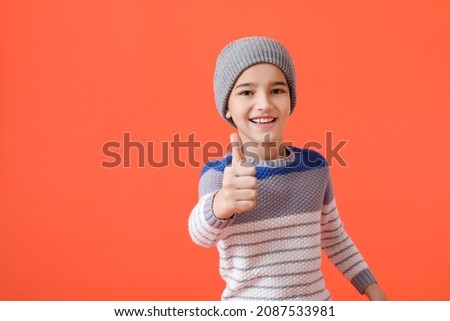 Stylish little boy in warm clothes showing thumb-up on color background