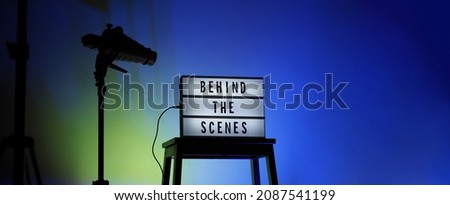 Behind the scenes text on Lightbox or Cinema Light box. Movie board light box on studio stair and light Snoot tripod on colors gradiant Background. Represent behind the scenes team is working on.
