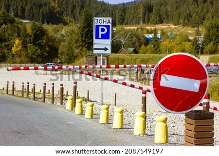 Parking in the open air. Red circular no-traffic sign and blue parking sign with text Parking area high up in the mountains in a pine forest. Red and white striped barrier prohibits entry. Fence posts