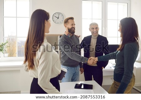 Happy business people meeting in a modern office. Two colleagues making an acquaintance and greeting each other. Friendly man and woman shaking hands after their coworkers have introduced them Royalty-Free Stock Photo #2087553316