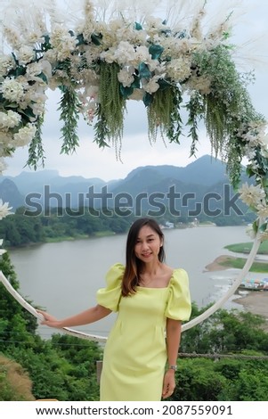 Asian woman with long hair dimples wearing a yellow dress Stand and pose at a beautiful vantage point surrounded by mountains and rivers.