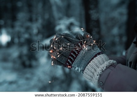 close-up on warm christmas mittens with lights around,it's cold outside,photo in the middle of a frozen forest