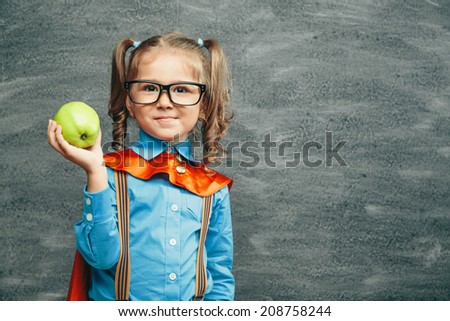 Cheerful smiling little kid (girl) against chalkboard. Looking at camera. School concept
