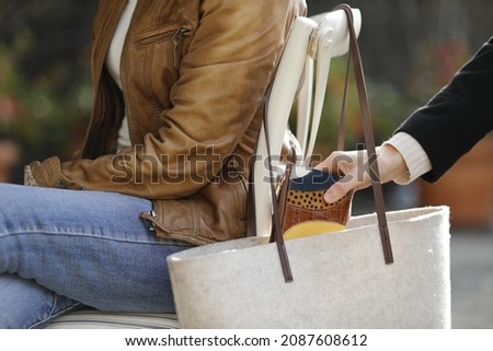 Thief stealing wallet from purse of a woman sitting on a terrace bar Royalty-Free Stock Photo #2087608612