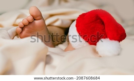 Banner kid's feet, Santa hat on a white bed. Infant baby is sleeping in his crib for holidays. Importance of sleep for babies. Sleep mode babies 3 y.o.