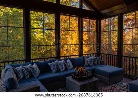 Cozy screened porch in early morning, rain drops on window and autumn leaves and woods in the background.