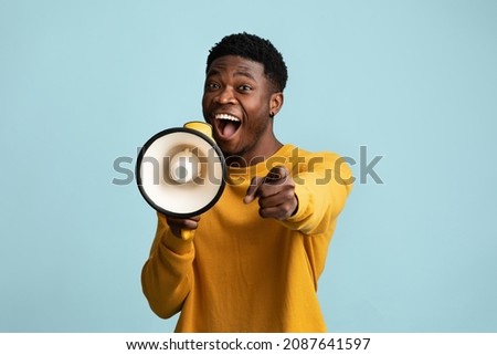 It is your chance. Emotional young black guy with megaphone making announcement on blue studio background, african american man saying something loud and pointing at camera, copy space Royalty-Free Stock Photo #2087641597