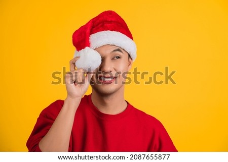 Portrait photo of handsome Asian man wearing christmas cap keeping holding white soft cotton ball in hand looking at side.