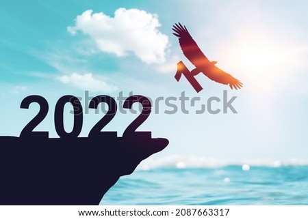 2022 new year concept with eagle bird flying away and holding number 1 on sunset sky background at tropical beach. Vintage tone filter effect color style.