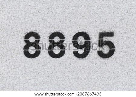Black Number 8895 on the white wall. Spray paint. Number eight thousand eight hundred ninety five.
