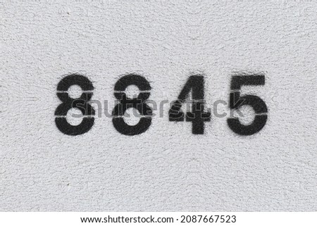 Black Number 8845 on the white wall. Spray paint. Number eight thousand eight hundred forty five.