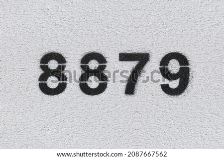 Black Number 8879 on the white wall. Spray paint. Number eight thousand eight hundred and seventy nine.